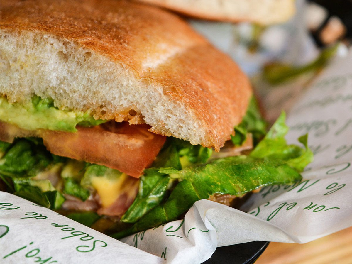 Torta de la casa servida en su papel, con aguacate, lechuga y tomate